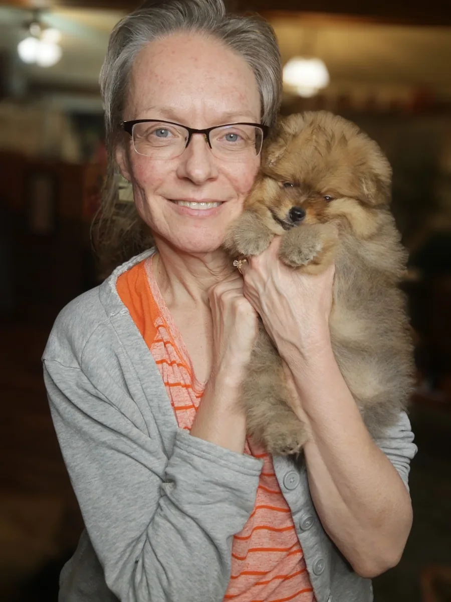 Linda Hodgens, smiling, holding a Pomeranian puppy against her cheek